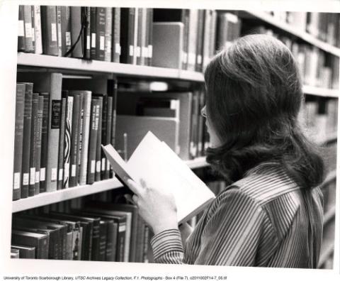 Student with book, browsing the library stacks