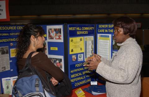 Student Speaks with Presenter at West Hill Community Services Table, Volunteer Fair, the Meeting Place