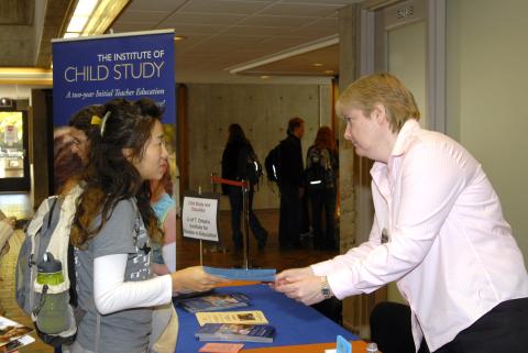 Student talks with Presenter at Table, Graduate and Professional Schools Fair, the Meeting Place