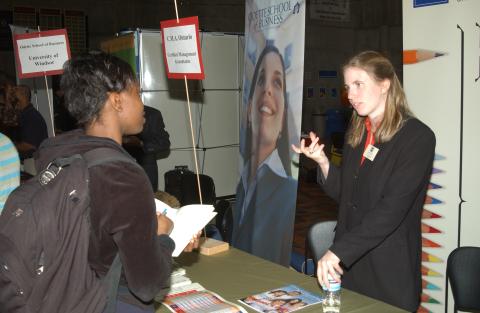 Student talks with Presenter at Table, C.M.A (Certified Management Accountants) Table, Graduate & Professional Schools Fair, the Meeting Place