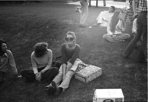 Students Sitting on Grass with Fire in Background