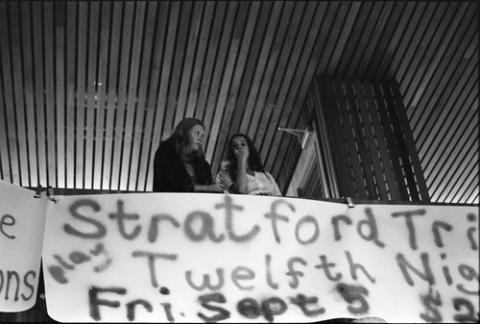 Two Students Standing on Balcony Above Hanging Signs