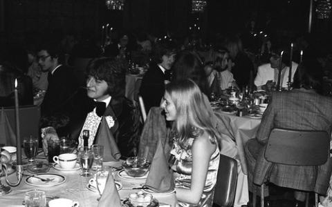 Two Students in Formal Wear Seated with Group at Dining Table