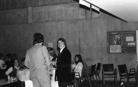 Students Standing and Seated by Tables in The Meeting Place